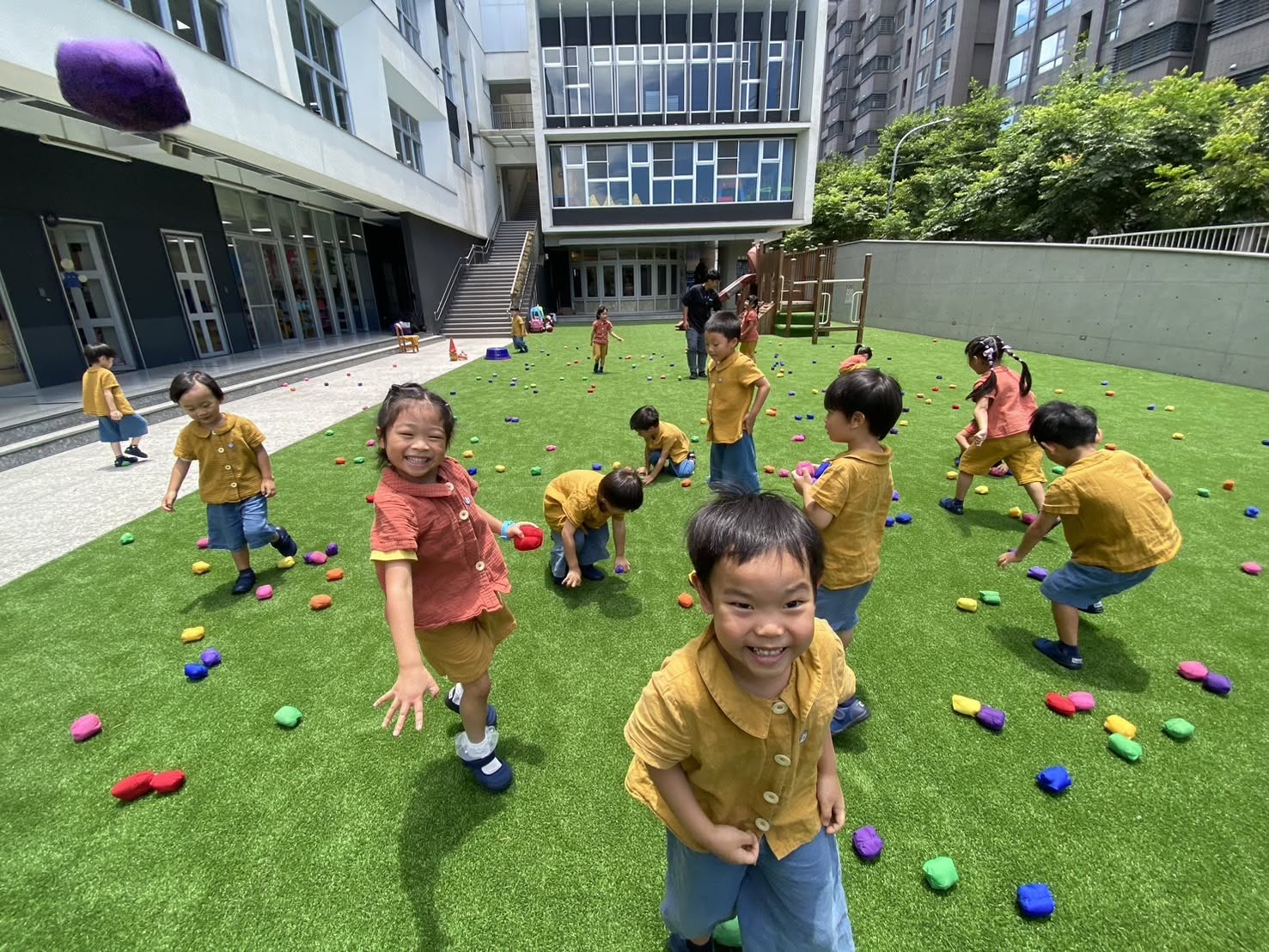 園區草地與校舍環境，孩子們在戶外撿拾彩色沙包