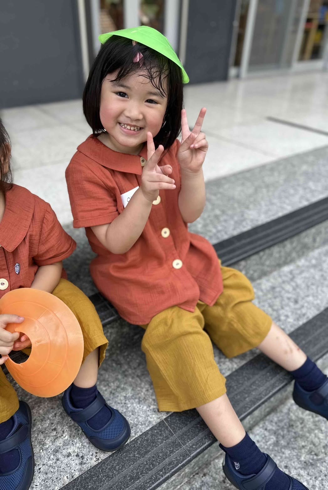 孩子坐在戶外階梯上開心比出手勢